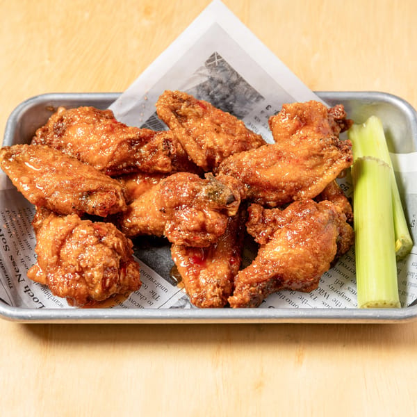 Granchio's crispy, glazed chicken wings with celery sticks, served on a metal tray with newspaper lining.