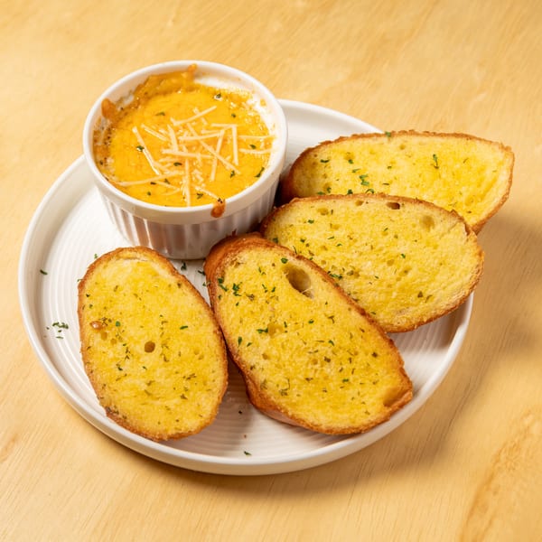 Granchio's cheesy seafood dip with shredded cheese and four slices of garlic bread on a white plate.