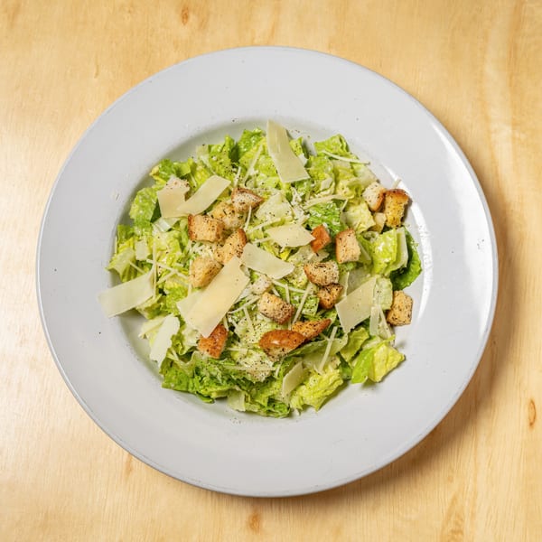 A Caesar salad with crisp lettuce, croutons, and shaved Parmesan cheese on a white plate.