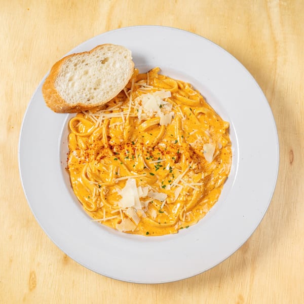 Granchio's creamy seafood pasta with parmesan cheese and a slice of bread on a white plate.