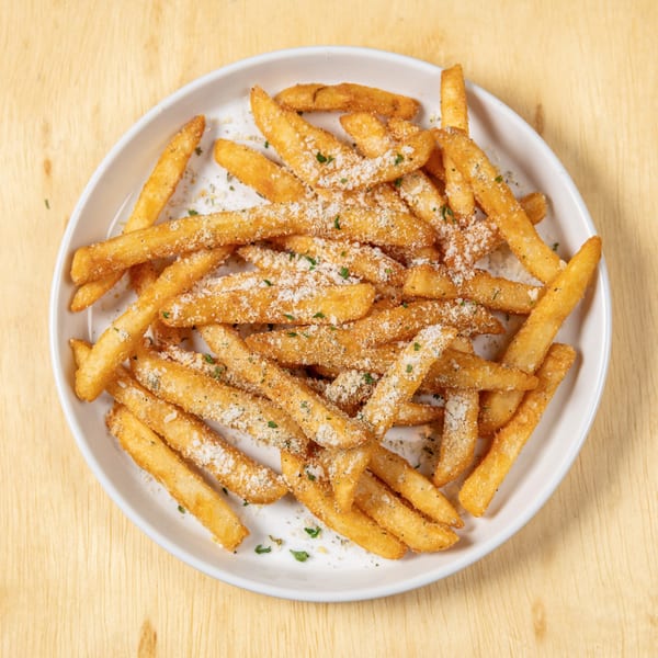 A white plate filled with golden french fries, sprinkled with parmesan cheese and herbs.