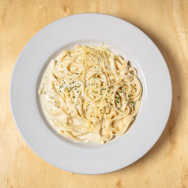 Creamy fettuccine alfredo pasta topped with shredded Parmesan cheese and parsley on a white plate.